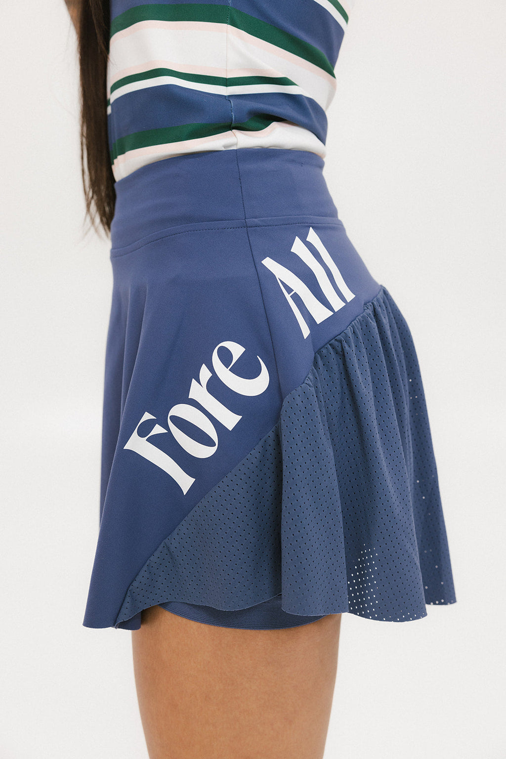 A person wearing a blue skirt with a mesh back, along with a striped top and white socks with green stripes. The image focuses on the skirt which has a sports-inspired design.